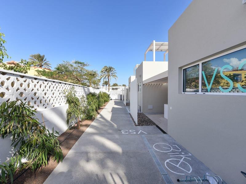 Hel verlichte hotelgang met planten en fietspad onder een blauwe lucht.