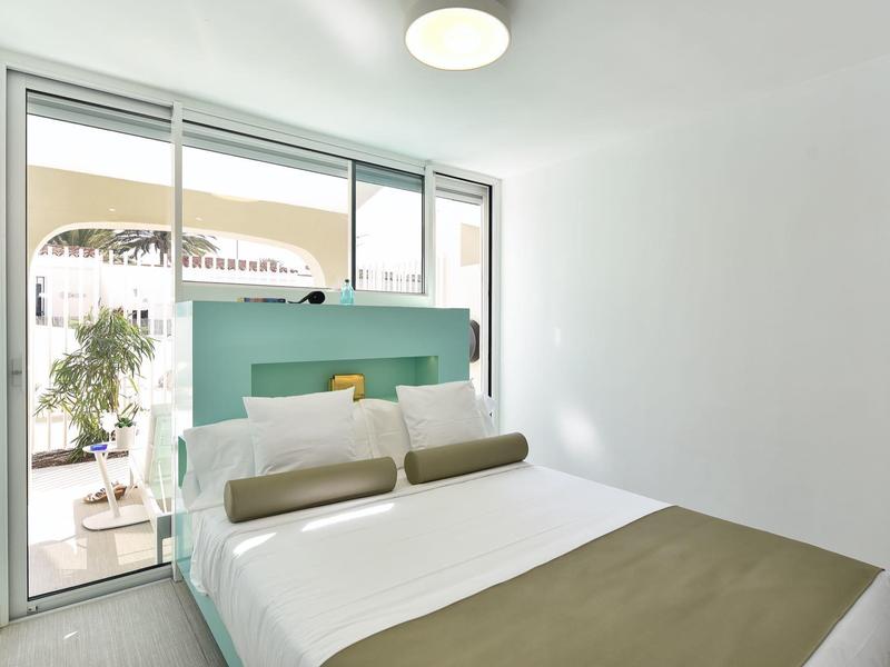 Moderne slaapkamer met tweepersoonsbed en terraszicht door grote glazen deuren.