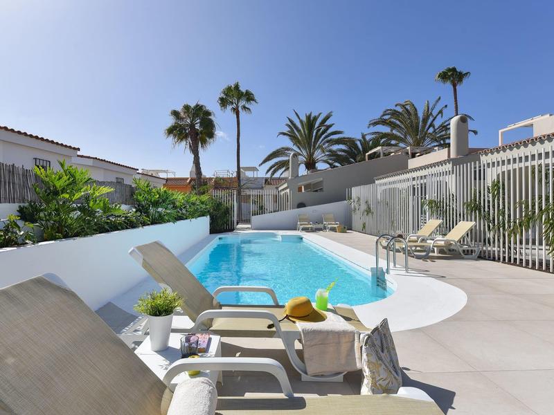 Moderne zwembadruimte met ligstoelen en palmbomen onder een heldere lucht.