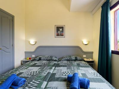 Eenvoudige slaapkamer met tweepersoonsbed, grijze kledingkast en open raam met gordijn.