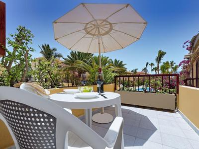 Terrasse avec table blanche, chaises et parasol surplombant des palmiers sous un ciel bleu.