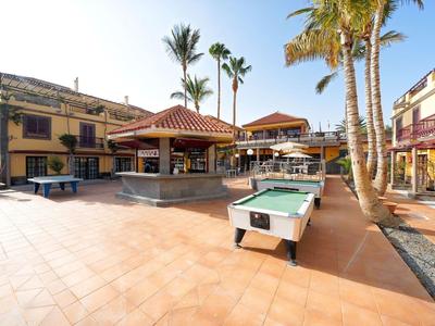 Buitengebied van het hotel met biljarttafels, palmbomen en zonneterras onder een heldere hemel.