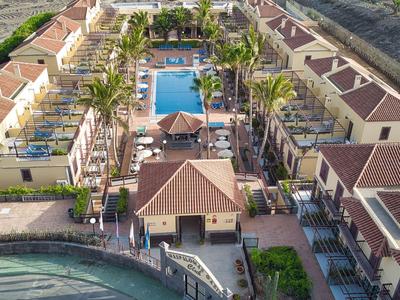 Vue aérienne d'un hôtel avec piscine, palmiers et bâtiments environnants au bord de l'eau