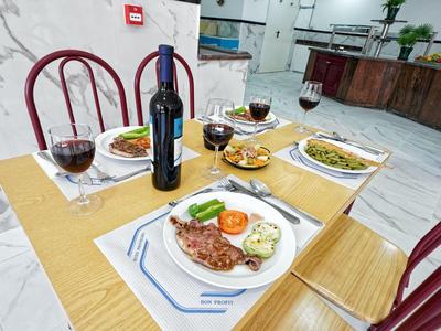 Gedekte tafel met wijnfles, vier glazen en borden met verschillende gerechten in een lichte restaurant.