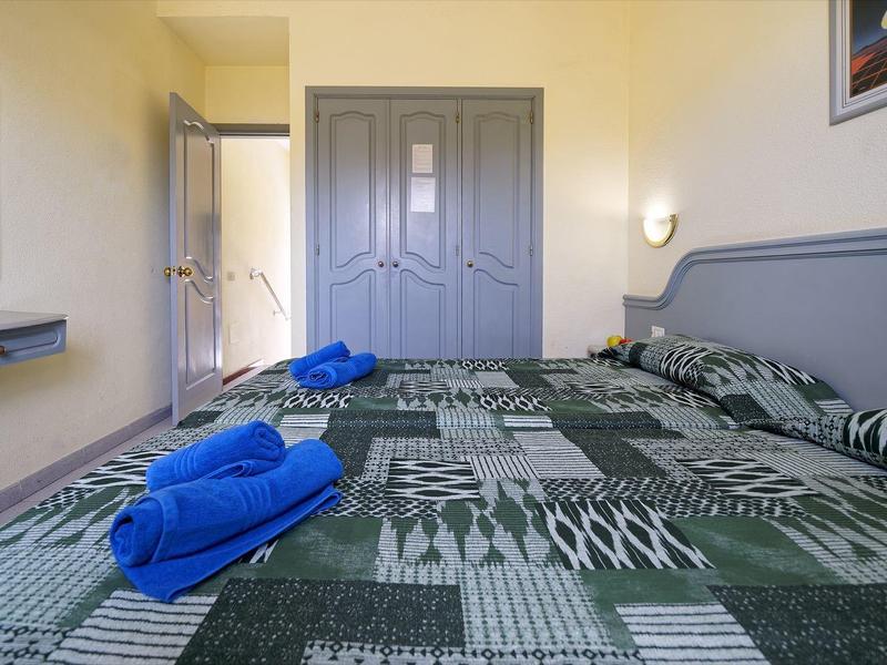 Gezellige hotelkamer met tweepersoonsbed, grijs meubilair en blauwe handdoeken.