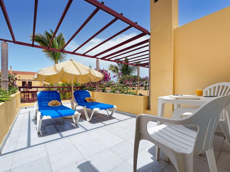 Balkon met twee blauwe ligstoelen en witte tuintafel met stoelen bij zonnig weer