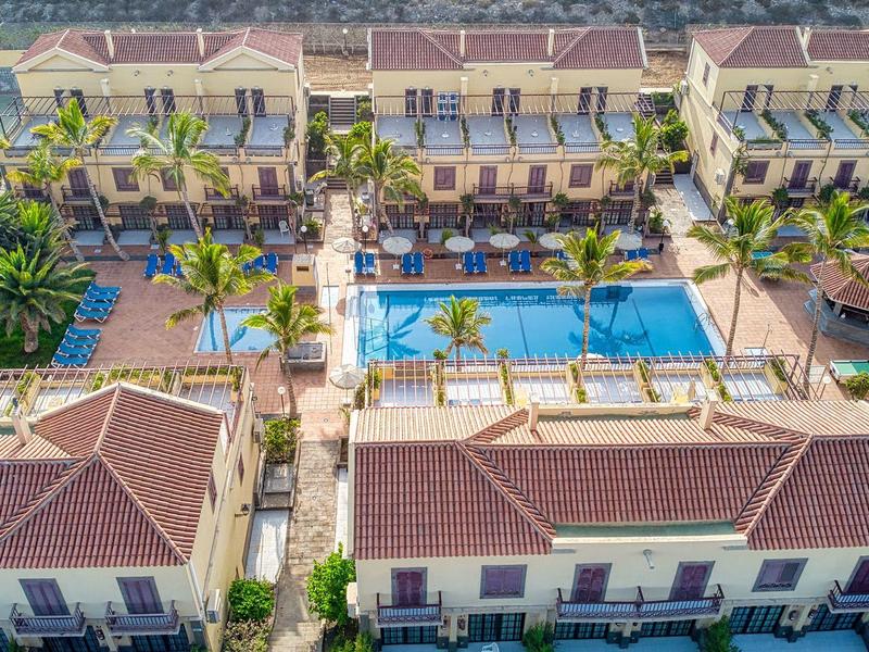 Hotelcomplex met twee lange zwembaden tussen rijen meerlaagse gebouwen met rode daken.