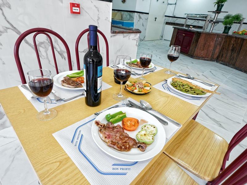 Gedekte tafel met wijnfles, vier glazen en borden met verschillende gerechten in een lichte restaurant.