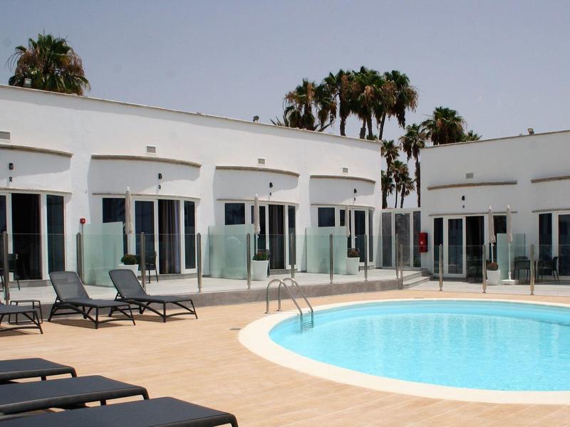 Moderní hotelový bazén s lehátky a přilehlými pokoji.