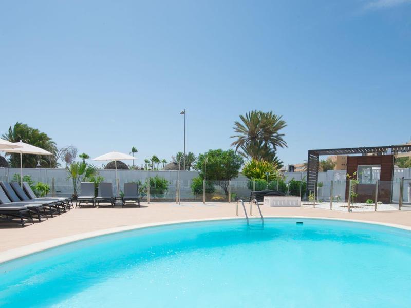 Kulatý bazén s modrými lehátky a bílými slunečníky na hotelové terase.