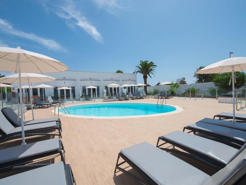 Kulový hotelový bazén s lehátky a slunečníky pod modrou oblohou.