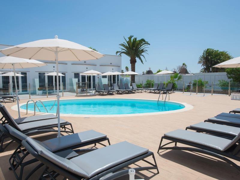 Moderní bazénová oblast s lehátky a slunečníky pod modrou oblohou.