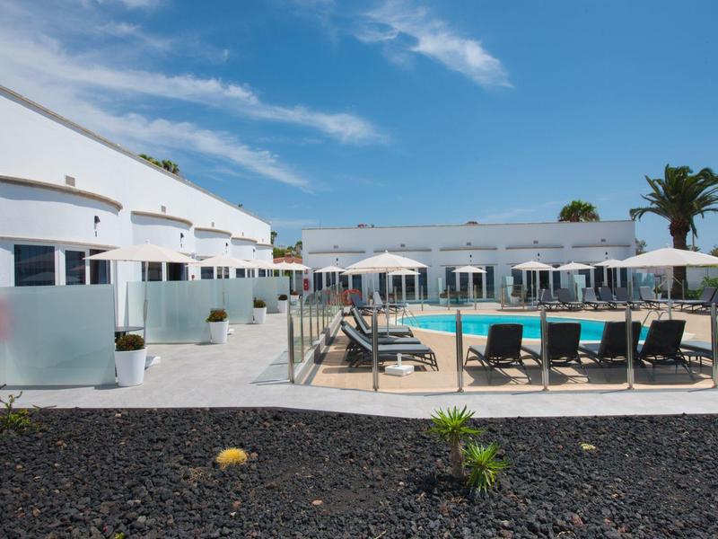 Moderní hotelový bazén s lehátky a slunečníky pod modrou oblohou.