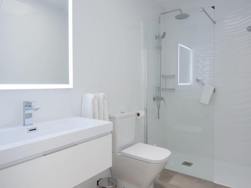 Moderní koupelna s bílým umyvadlem, toaletou a skleněným sprchovým koutem.