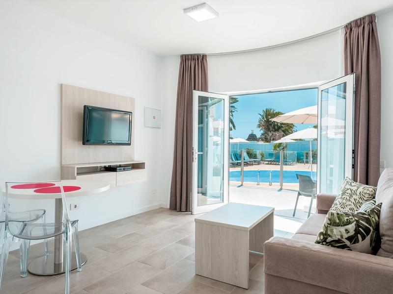 Moderní hotelový pokoj se dveřmi na terasu k bazénu a posezením.