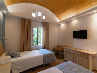 Hell gestaltetes Schlafzimmer mit zwei Betten, Holzmöbeln, TV und Bogenfenster mit Vorhängen.