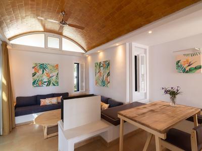 Helles Wohnzimmer mit zwei Sofas, Holztisch, weißen Stühlen, bunten Bildern und Lehm-Bogendecke.