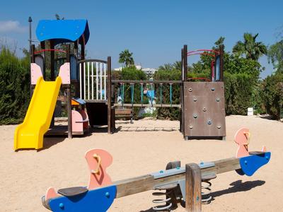 Kinderspielplatz mit gelber Rutsche, Kletterwand, Schaukeln und Wippe auf Sandboden.