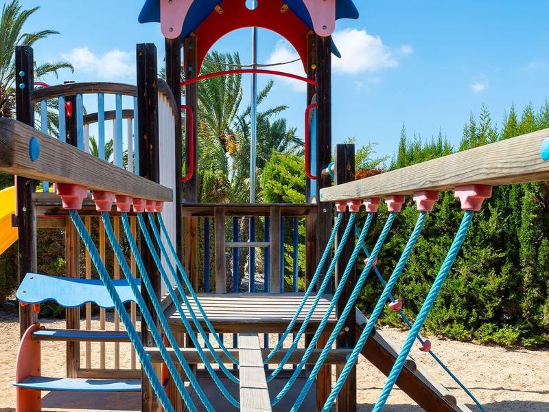 Ein Klettergerüst mit Seilschlaufen, Holzplattform und Rutsche auf einem Sandspielplatz.