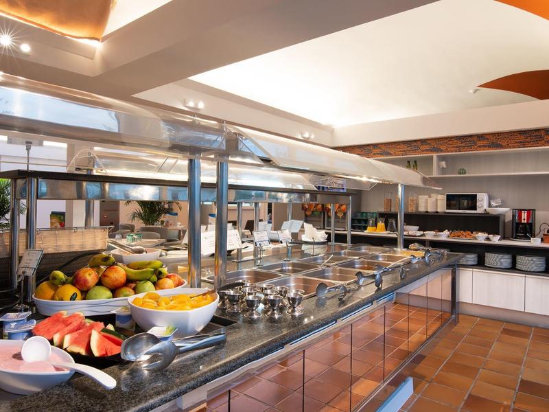 Buffet mit verschiedenen Obstsorten, Salaten und warmen Speisen in modernem Speisesaal.