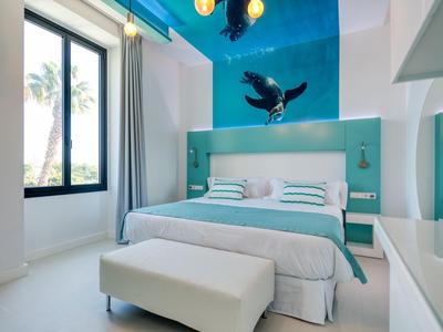 Camera d'hotel moderna con letto matrimoniale, accenti turchesi e grande finestra con vista sulle palme.