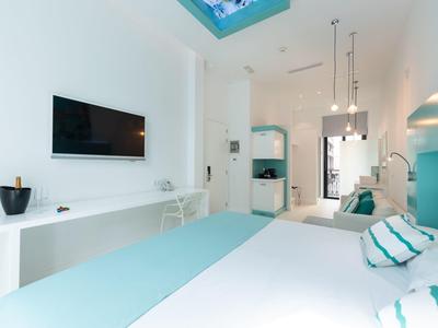 Camera d'hotel luminosa con mobili bianchi moderni, letto matrimoniale e accenti blu sotto una finestra sul tetto.