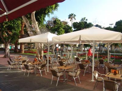 Terrazza esterna di un bar con tavoli, sedie e ombrelloni in una giornata di sole.