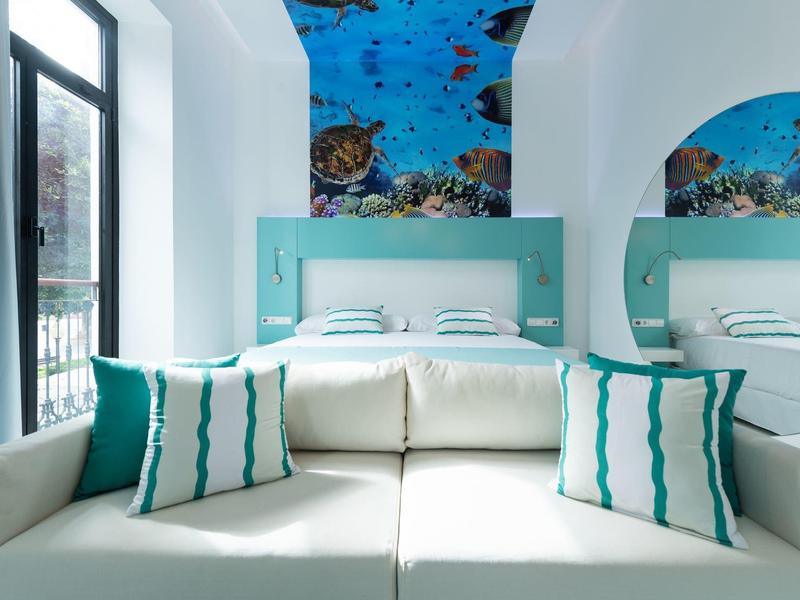 Camera d'hotel moderna con divano, cuscini turchese e bianco e soffitto dipinto.