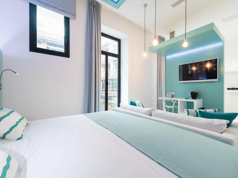 Camera d'hotel moderna con letto matrimoniale, TV e molta luce naturale.