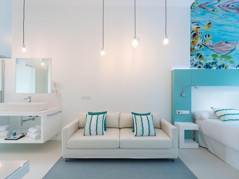 Camera d'hotel luminosa e moderna con divano, letto e decorazioni ispirate al mare.