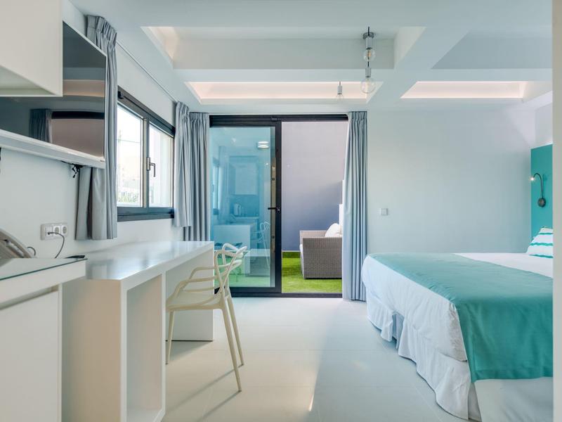 Camera d'hotel luminosa con letto matrimoniale, angolo cottura e balcone con posti a sedere, design moderno.