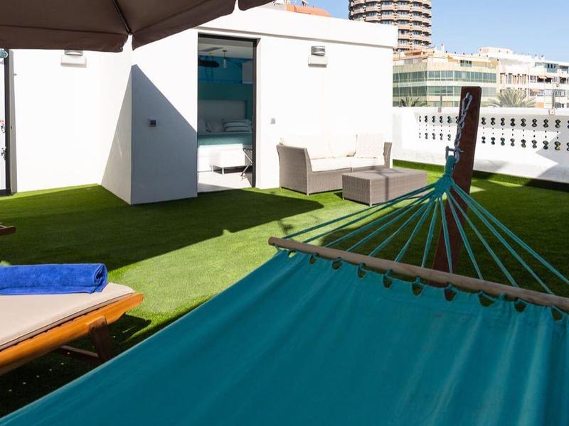 Terrazza sul tetto con amaca, lettini e prato artificiale sotto un cielo blu.
