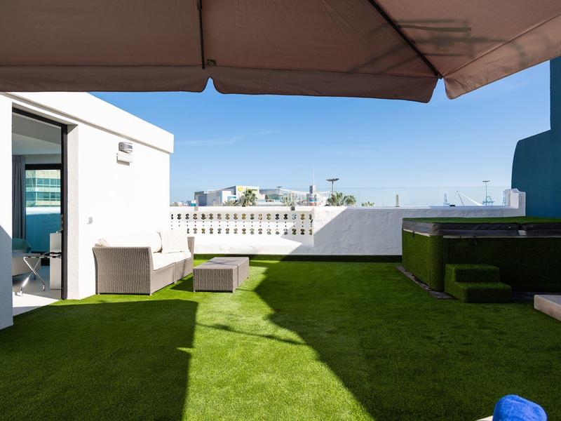 Terrazza sul tetto con prato artificiale, area salotto e vista sulla città sotto un cielo sereno.