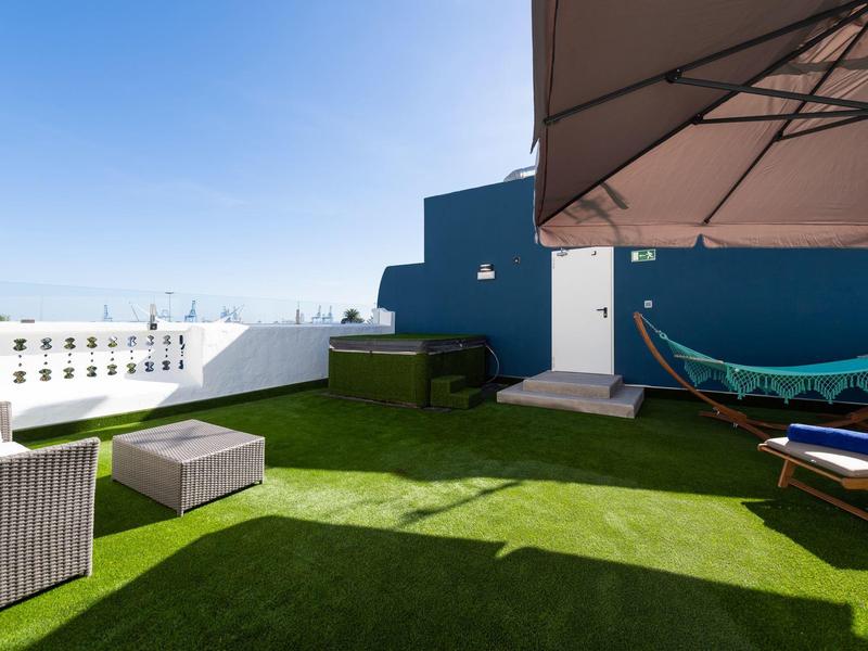 Terrazza sul tetto con erba sintetica verde, mobili da salotto e amaca sotto un cielo blu.