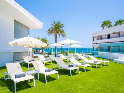 Zonnig hotelterras met witte ligstoelen en parasols naast een zwembad.