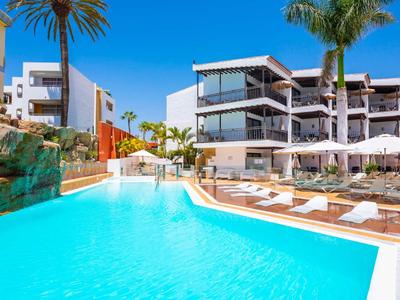 Modern hotelzwembad met ligstoelen en palmbomen onder een heldere blauwe lucht.