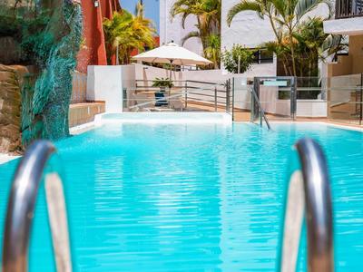 Klarer blauer Pool mit Metallgeländern und Liegestühlen im Hintergrund eines Hotels.