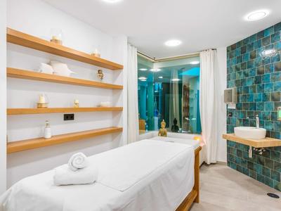 Lichte spa-kamer met massagetafel en planken met kaarsen en handdoeken.