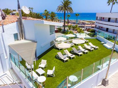 Blick auf eine Terrasse mit Sonnenliegen und Sonnenschirmen, im Hintergrund das Meer und Palmen.