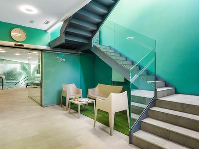 Moderne entree met trap, glazen leuning en beige zitgedeelte tegen een groene muur