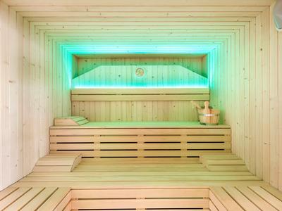 Heldere houten sauna met groene verlichting en traditionele saunabenodigdheden.