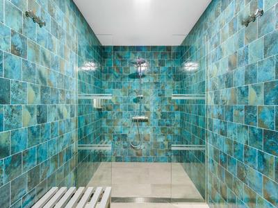 Grote douche met blauwgroene tegels en witte planken, modern en schoon.