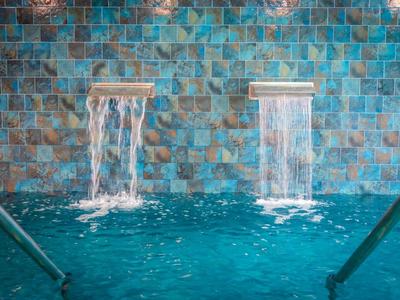 Twee watervallen stromen in een zwembad met turquoise tegels op de achtergrond.