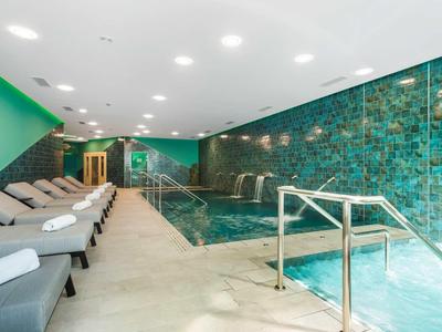 Binnenzwembad met groene muren, ligstoelen en leuningen in de hotelspa.