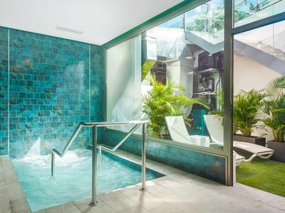 Moderne wellnessruimte met bubbelbad, glazen deur en ligstoelen naast een groen grasveld.