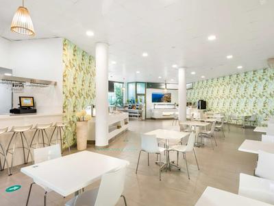 Lichte, moderne eetruimte met witte tafels, stoelen en botanisch patroon op de muur.