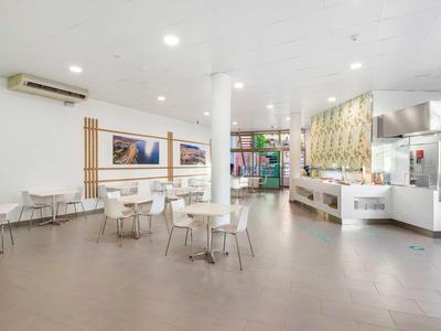 Lichte, moderne hotel-loungesruimte met tafels, stoelen en decoratief wandontwerp.