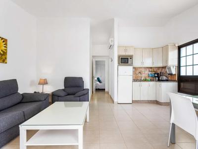 Woonkamer met grijze bank, fauteuil, witte tafel en geïntegreerde keuken in lichte ruimte