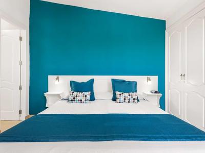 Moderne hotelkamer met tweepersoonsbed, turquoise muur en witte meubels.