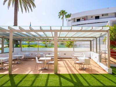 Ontspanningsruimte met overdekte zitplaatsen, grasveld en uitzicht op water en palmbomen.